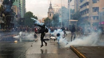 Protester throwing object in the middle of a street with protesters and tear gas in the background.