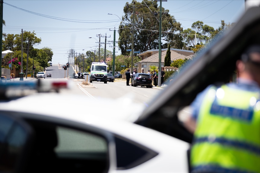 A police officer and police vehicle blurred out in the foreground with an ambulance and vehicle down a street in the background.