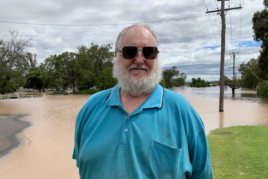 A man wearing a blue polo shirt and black sunglasses standing in front of a flooded street.