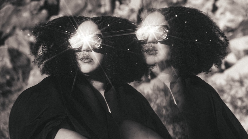 Black and white photo of Brittany Howard wearing kaleidoscopic goggles with a mirror image
