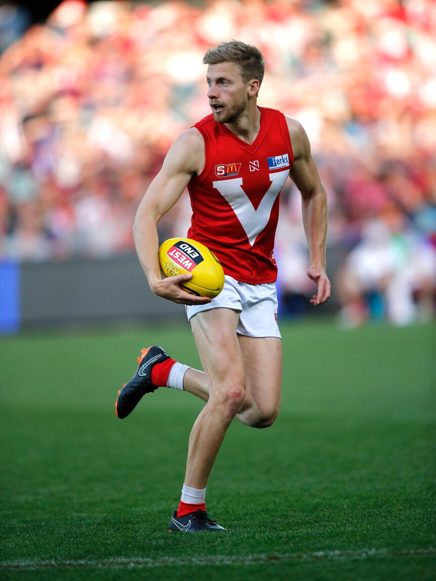 A blonde white man holding a football at Adelaide Oval in the 2018 SANFL Grand Final. 