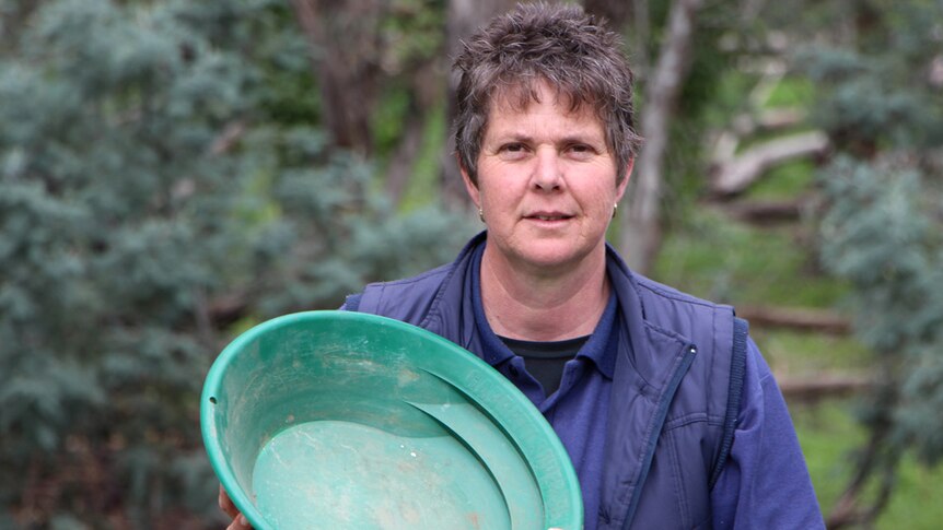 A lady in a blue vest holding a green gold mining pan