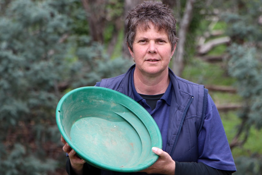 A lady in a blue vest holding a green gold mining pan