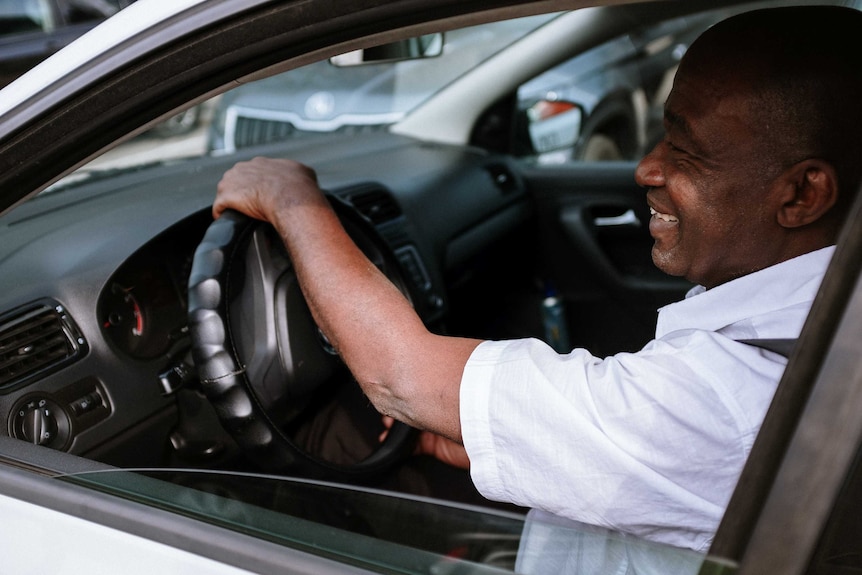 A man in a white shirt drives a car with the window down, for a story about green driving.