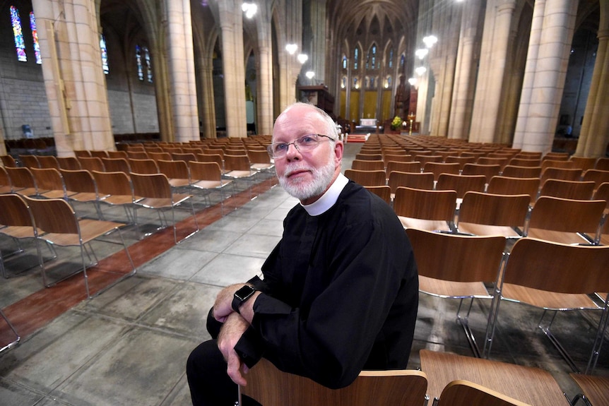 Dr Peter Catt sits inside St John's Anglican Cathedral, with the cathedral interior behind him.