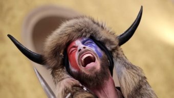 A man wearing a horned fur hat holding a spear yells inside the US Capitol Building while holding a spear.