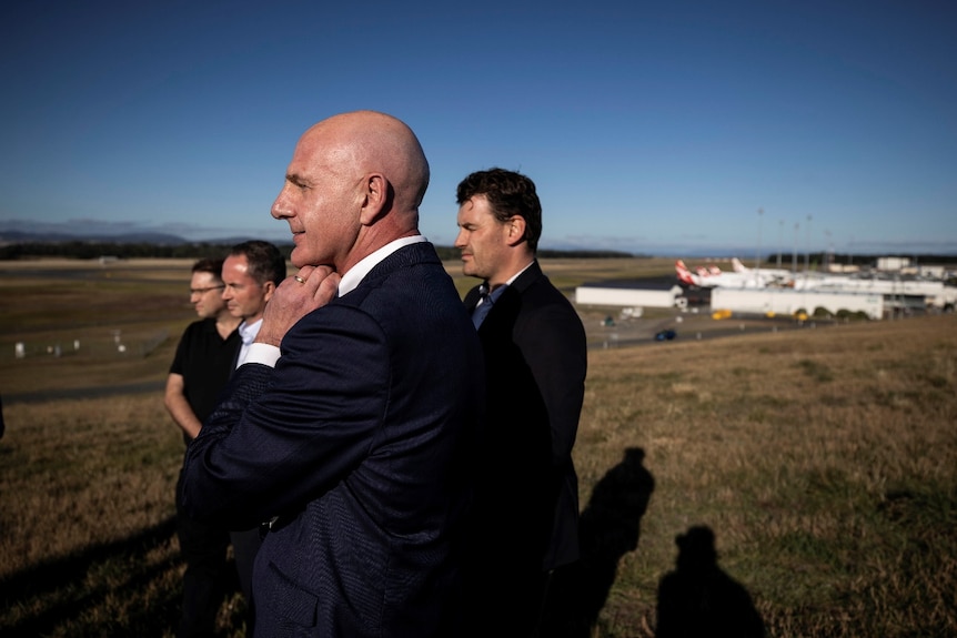 Four men stand in a row with several planes in the background.