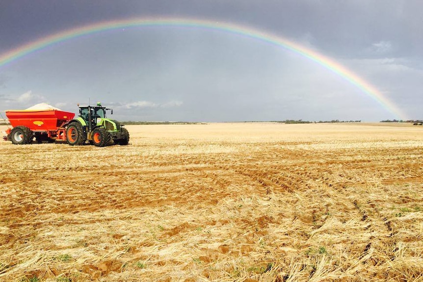 A tractor on a crop with a rainbow in the background.