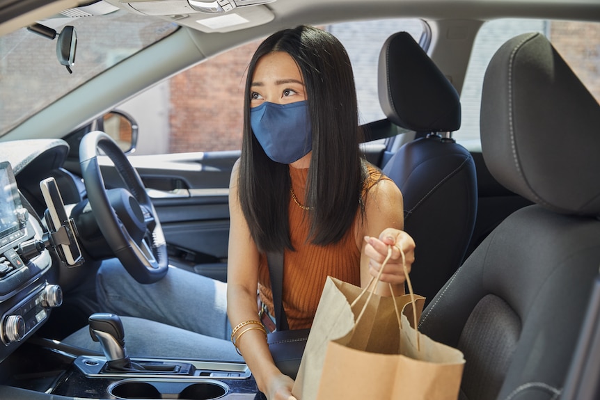 Masked delivery driver in a car with a bag of takeaway food. 