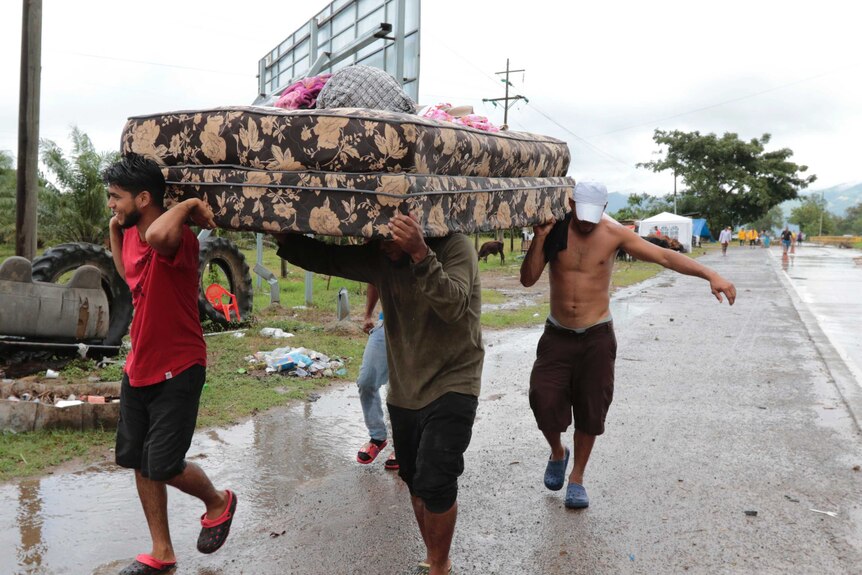 Men carry mattress in the rain.