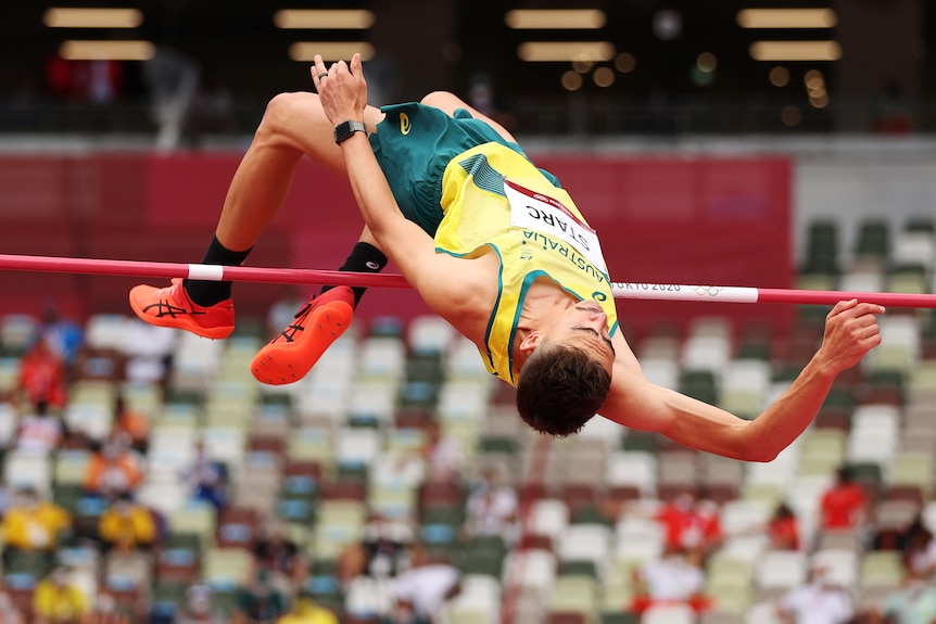 A man wearing a yellow single jumps over a red bard