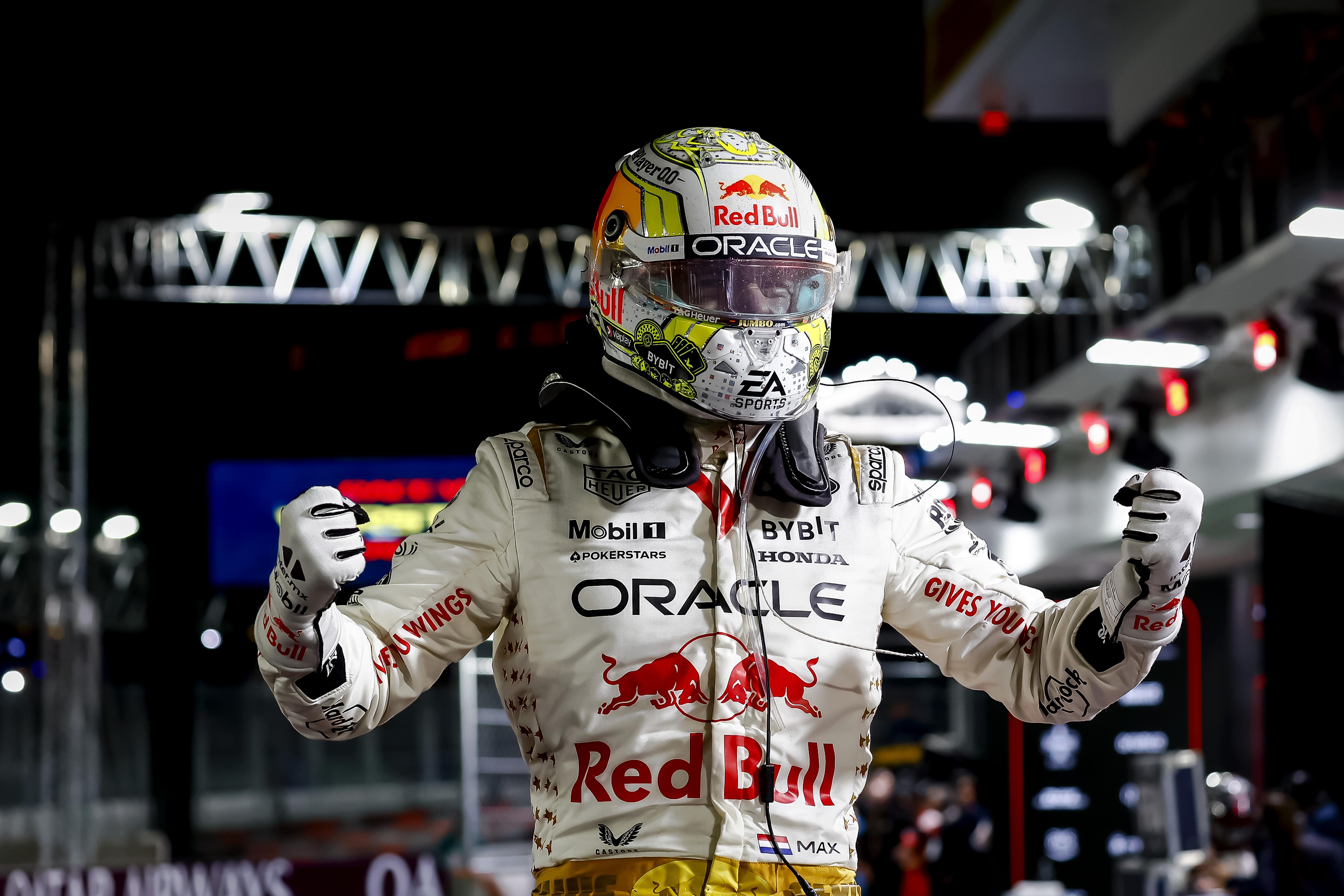An F1 driver in a white race suit, punches the air in celebration, at night.