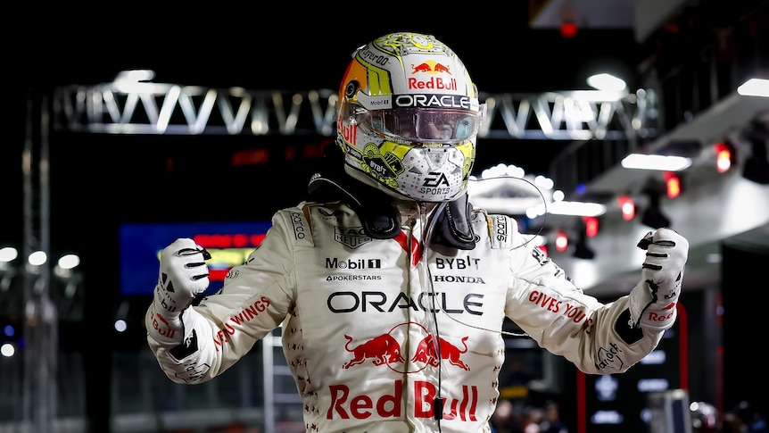 An F1 driver in a white race suit, punches the air in celebration, at night.