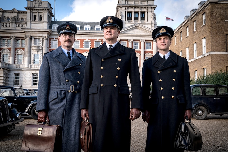 Three middle-aged men, wearing military uniforms, stand looking determined and holding luggage in a London street