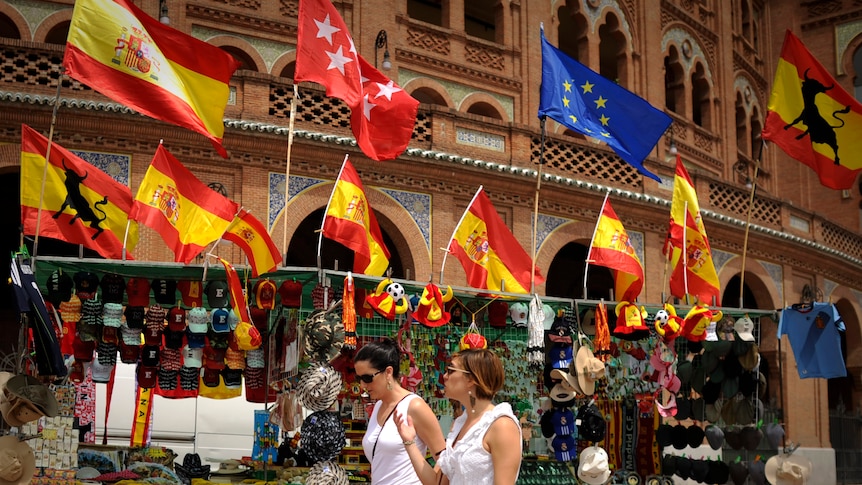 Two women walk past a stall in Madrid selling Spanish flags.