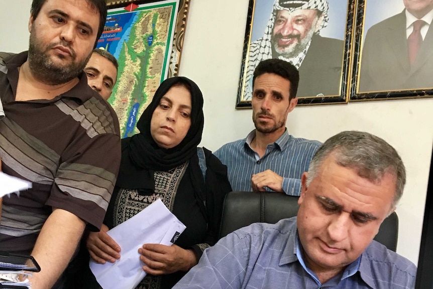 Four people wait at the desk of an official who is stamping paperwork.