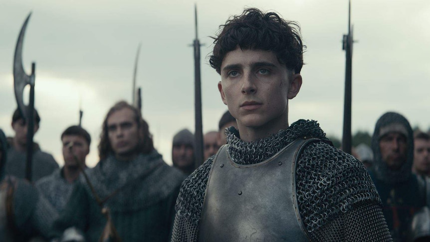 The actor Timothée Chalamet playing King Henry in chain mail and armour on a battlefield