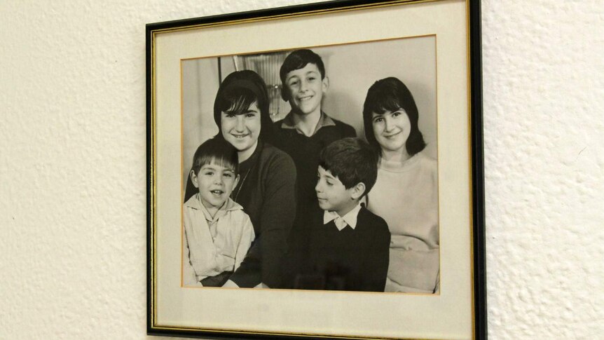 A framed black and white photograph of the five Paxinos children smiling at the camera.