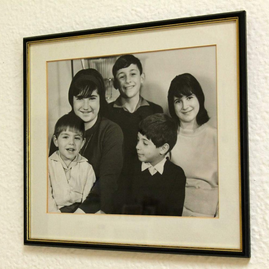 A framed black and white photograph of the five Paxinos children smiling at the camera.
