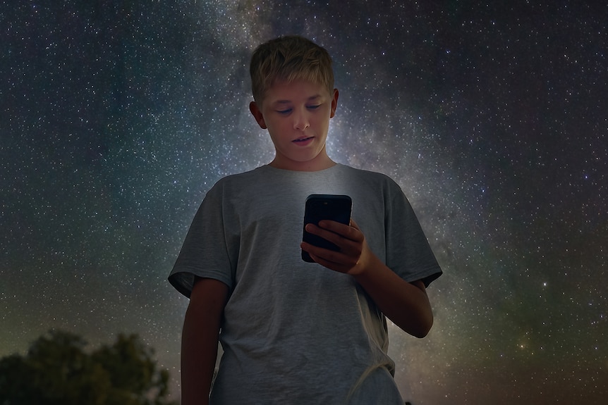 A young person is looking down at his phone with the stars above