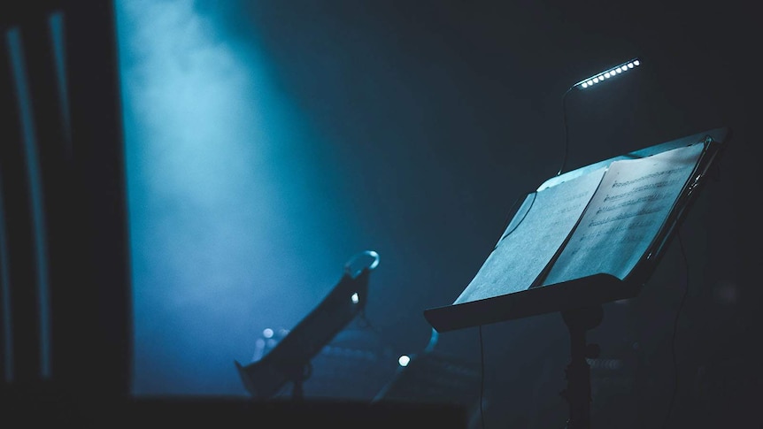 A lit music stand sits in the wings of a theatre