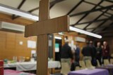A cross can be seen in focus at the forefront of the photo. People blurred in the background.