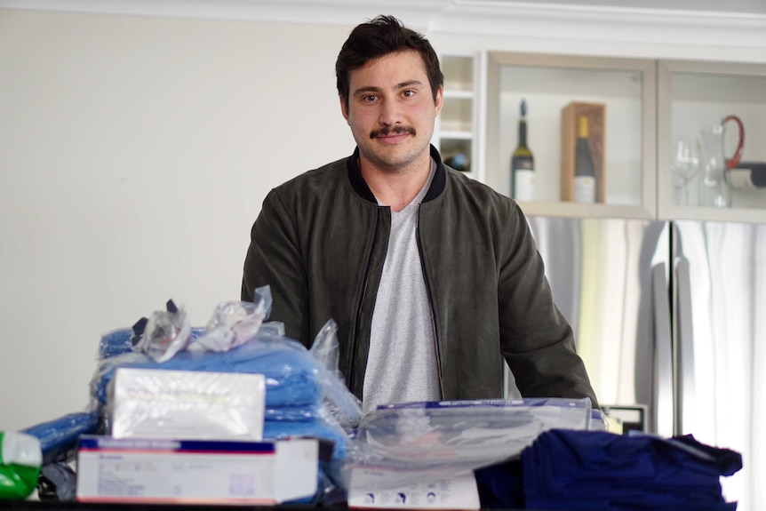 Justin Holland standing behind a pile of clothes and medical protective gear