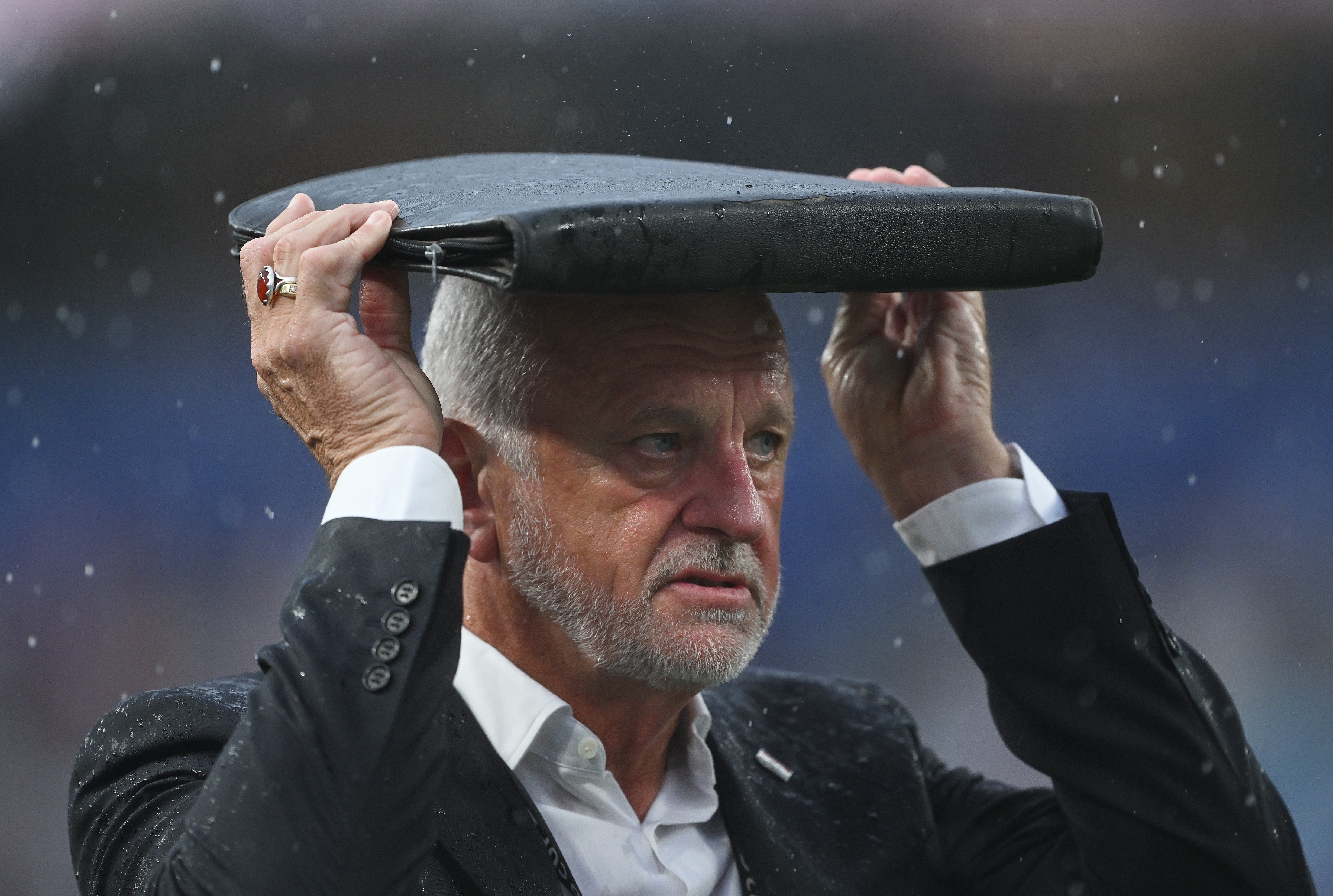 Graham Arnold holds a clipboard on his head to shelter from the rain.