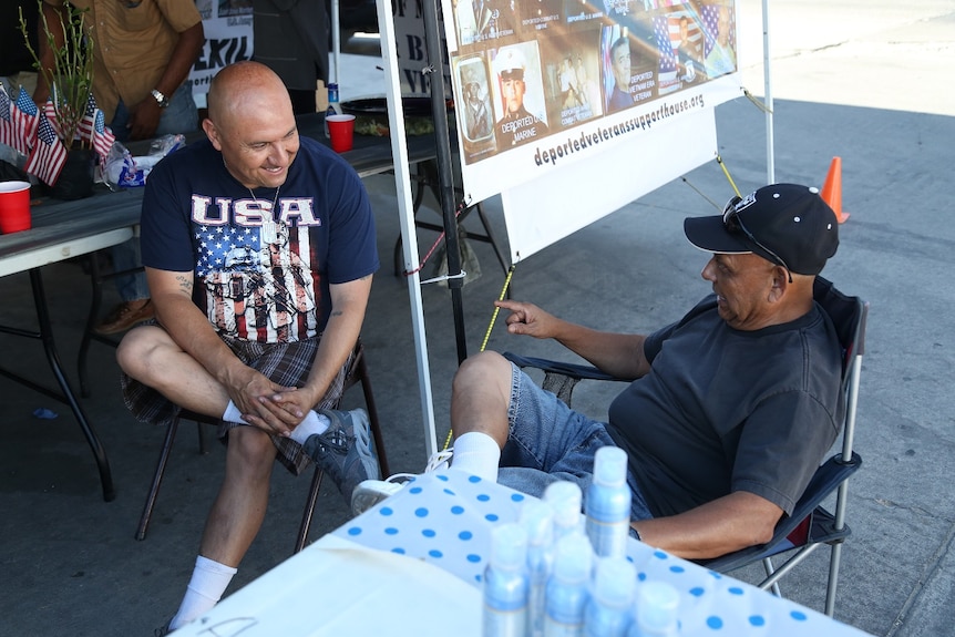 Two men sit on camping chairs while having a chat.