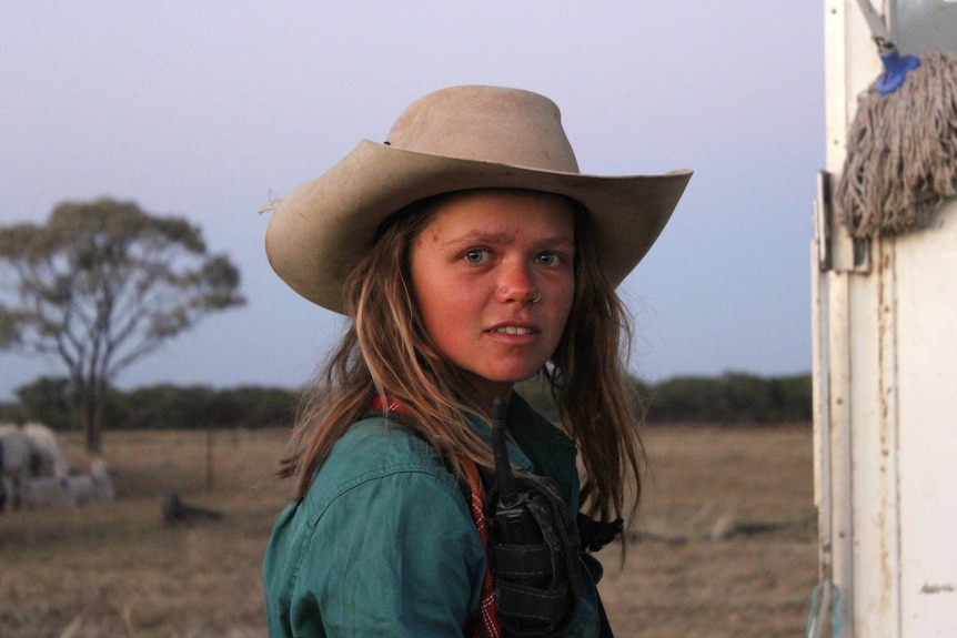 A young woman with a cowboy hat looks directly at the camera
