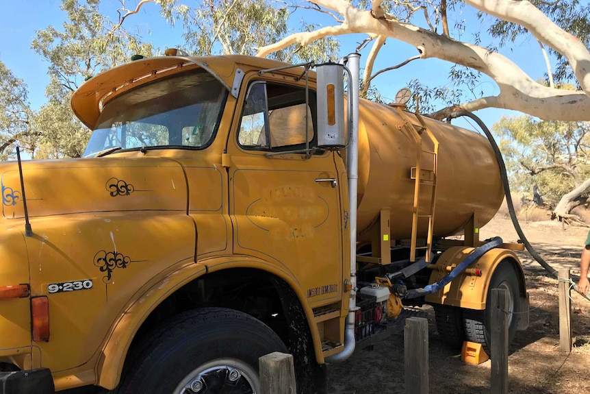 A full shot of an old, yellow truck. It has a water tank on the back.