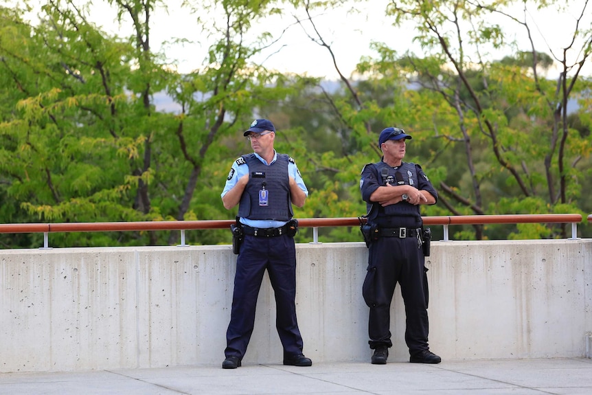 Two policemen stand in front of trees outside Parliament House