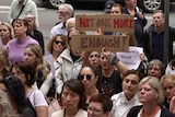 A crowd of protesters, with one holding a sign reading 'enough is enough'.