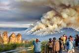 People watch from a lookout as smoke rises from a bushfire in a forested valley