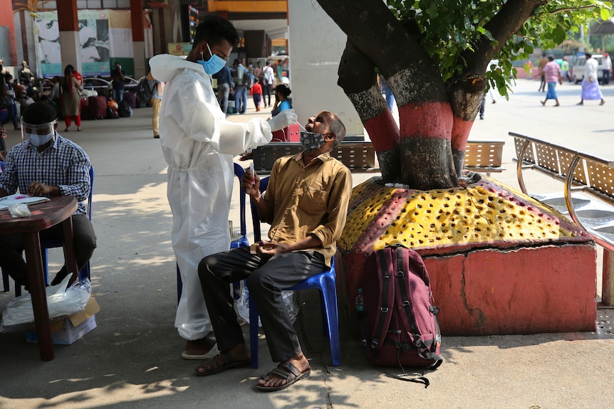 A man reacts as a health worker takes his mouth swab sample by a street stall.