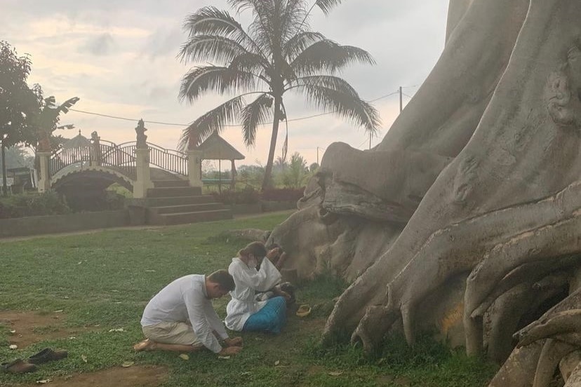 Two people crouch in front of a tree to pray