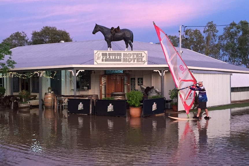 a man stands on a wind surfer outside a hotel where flood water has risen to the front of