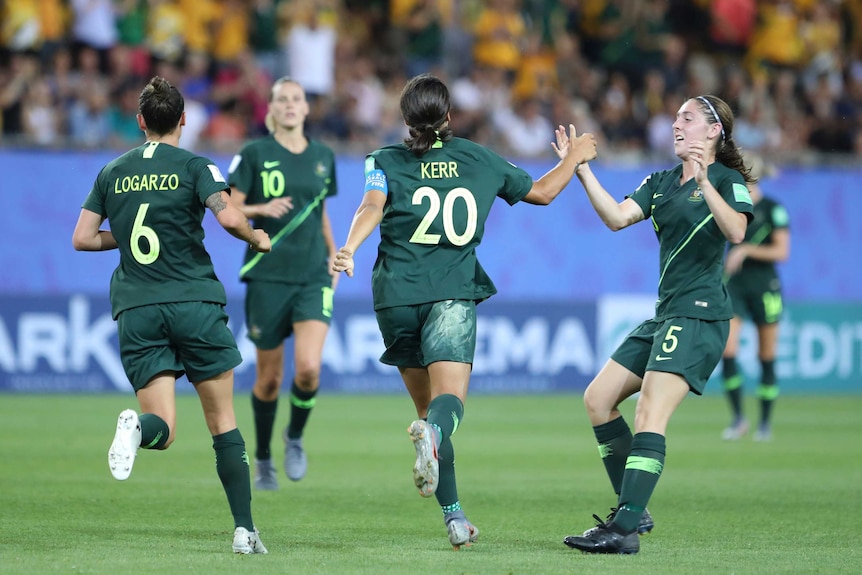 Sam Kerr celebrates a goal by giving a high five to a teammate as she runs away from the camera