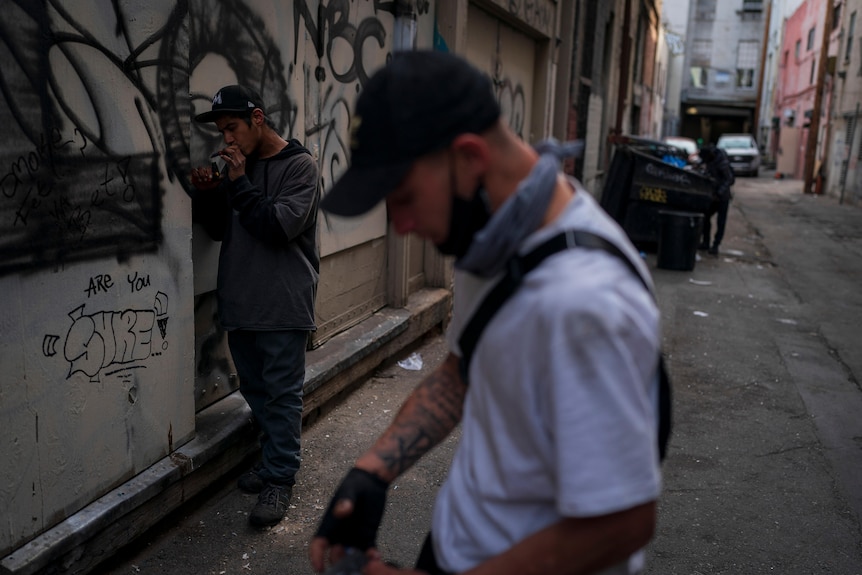 two men in a an alleyway smoking and preparing to smoke fentanyl