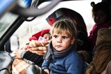 A young, blonde-haired child sits in the front seat of a car fleeing Idlib in Syria.