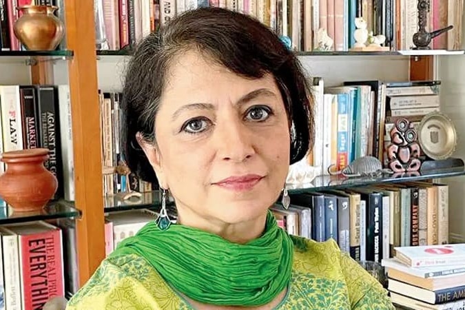 woman with brown hard and wearing green saree standing in front of book shelf