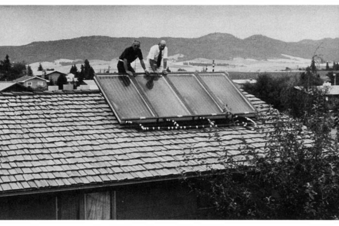 Black and white photo of two men leaning on a rooftop solar panel.