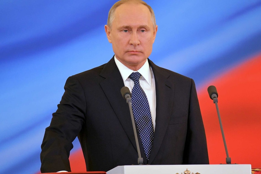 Putin is seen standing on a podium, his hand on the constitution.