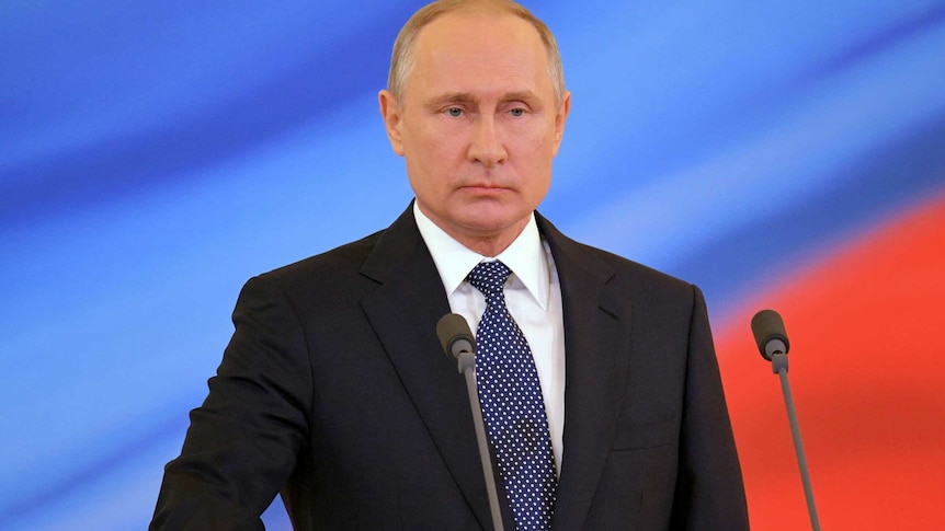 Putin is seen standing on a podium, his hand on the constitution.