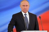 Putin is seen standing on a podium, his hand on the constitution.