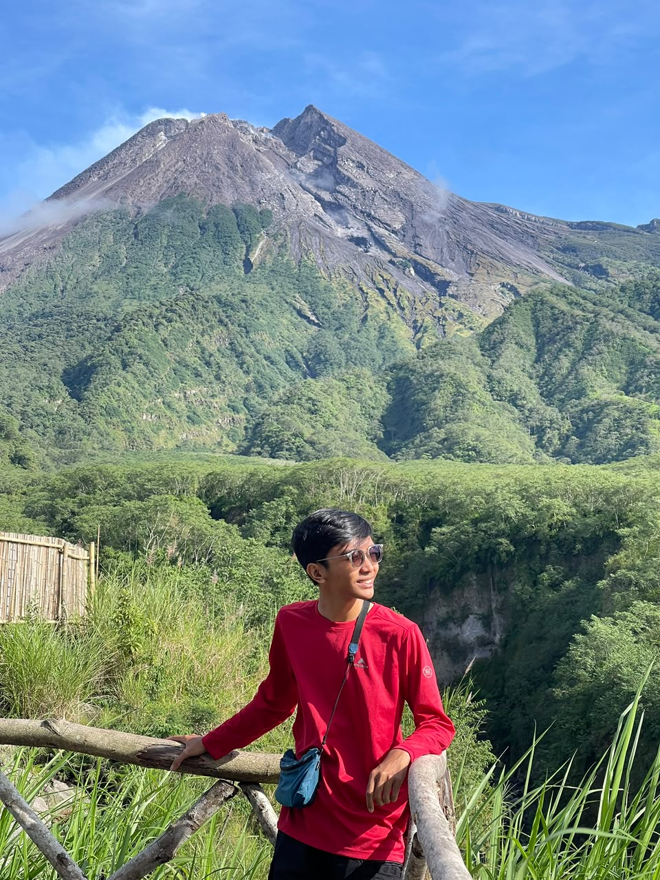 A man wearing glasses and hat posing near a volcano