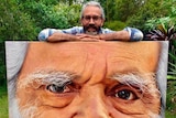 Man standing behind portrait that stands about one metre square.