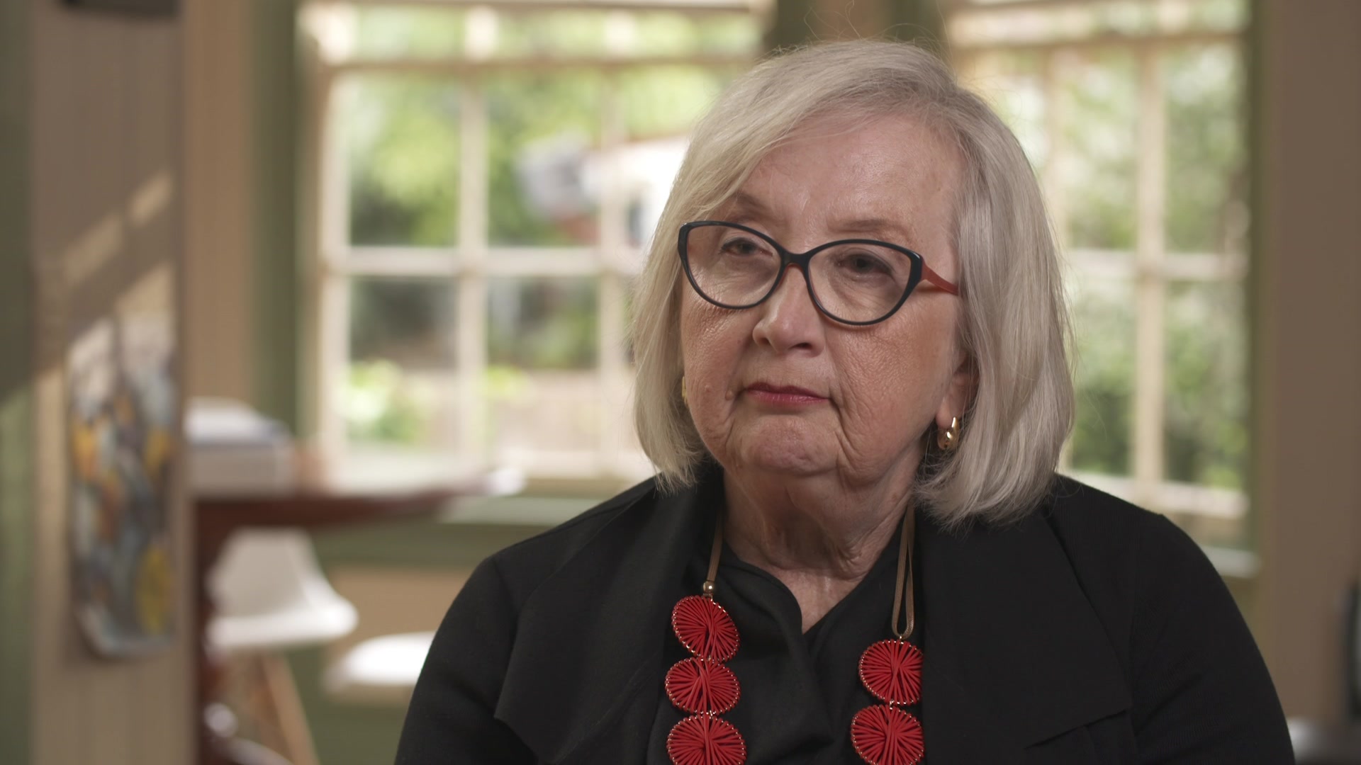 Anne Hollands, wearing a black shirt and bright red necklace. 