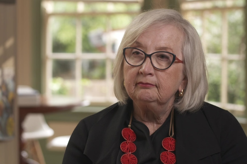 Anne Hollands, wearing a black shirt and bright red necklace. 