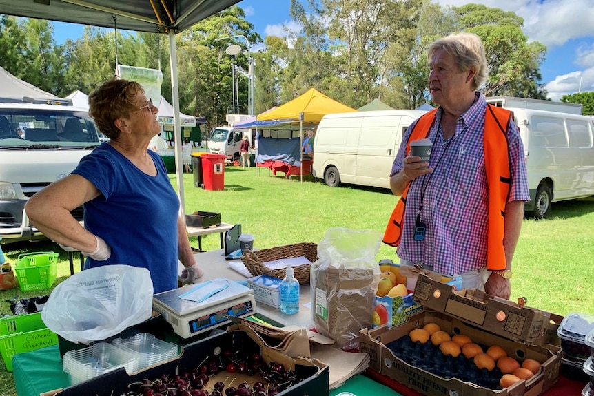 A man and a woman talk at a market stall.